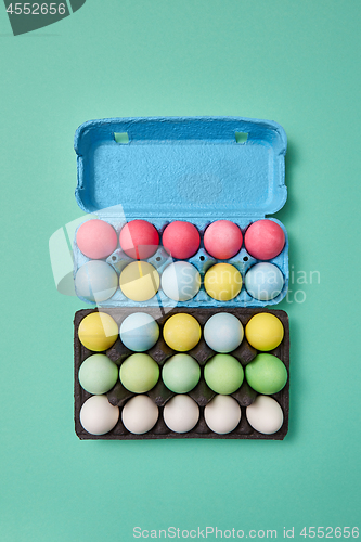 Image of Multi-colored bright Easter eggs in a blue and black cardboard box on a green background with copy space. Easter layout for your ideas. Flat lay