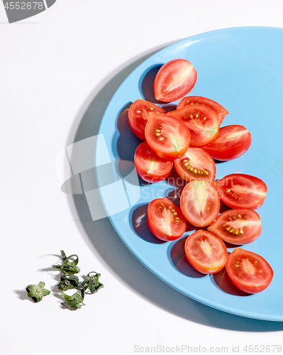 Image of Halved ripe tomatoes in a blue plate on a gray background with shadows and copy space. Ingredients for salad. Top view