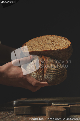 Image of male baker holding in hands halves of fresh rye bread,