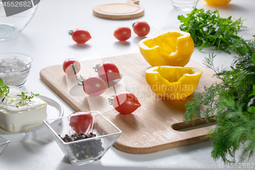 Image of Ingredients for salad preparation, cheese, tomatoes, peppers, greens on a white kitchen table.