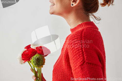 Image of Happy girl in a red knitted sweater with a beautiful bouquet of brightly colored Ranunculus flowers around a gray background with copy space.