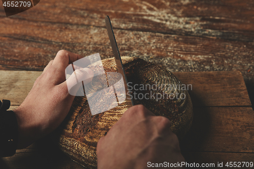 Image of A man baker cuts bread