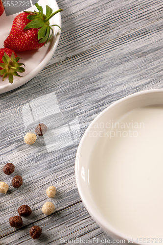 Image of Ripe strawberries, cereal balls and a plate of milk on a gray wooden table. Top view