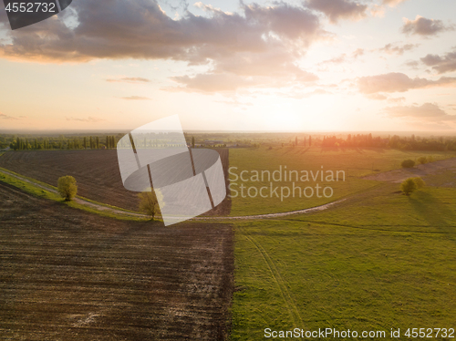 Image of Aerial view from the drone, a bird\'s eye view of abstract geometric forms of agricultural fields with a dirt road through them in the summer evening at sunset.