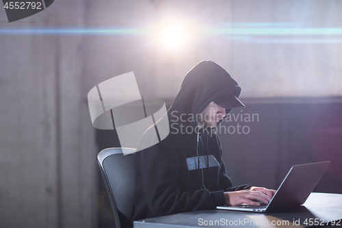 Image of young talented hacker using laptop computer while working in dar