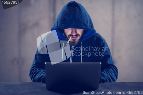 Image of young hacker using laptop computer while working in dark office