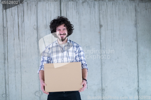 Image of casual businessman carrying cardboard box in front of a concrete