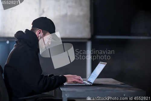 Image of talented hacker using laptop computer while working in dark offi