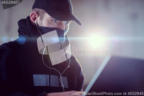 Image of young talented hacker using laptop computer while working in dar