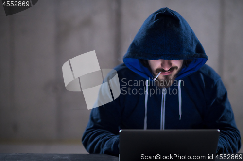 Image of young hacker using laptop computer while working in dark office