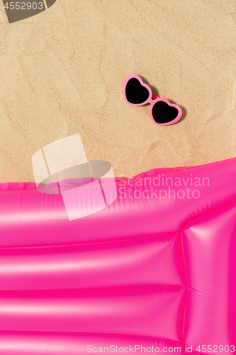 Image of sunglasses and pink swimming mattress on beach