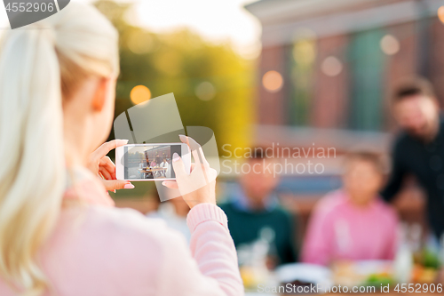 Image of woman photographing friends by smartphone at party