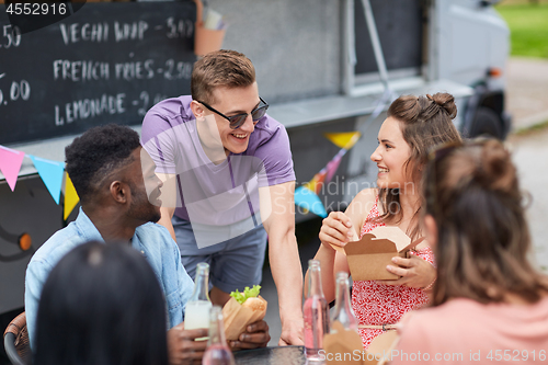 Image of happy friends with drinks eating at food truck