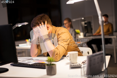 Image of stressed man at computer monitor at night office