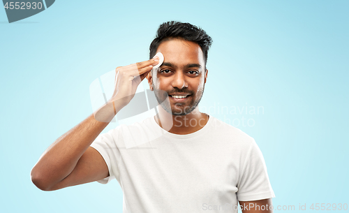 Image of smiling indian man cleaning face with cotton pad