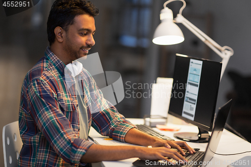 Image of creative man with laptop working at night office