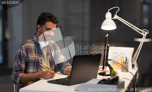 Image of creative man with laptop working at night office
