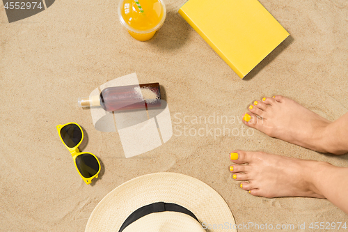 Image of feet, hat, shades, sunscreen and juice on beach