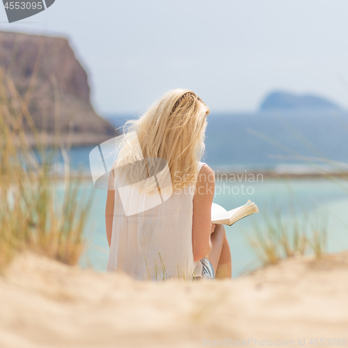 Image of Woman reading book, enjoying sun on beach.