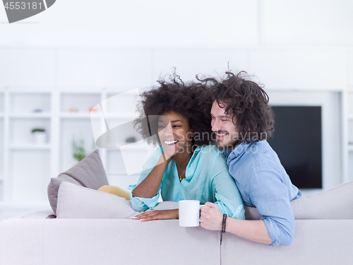 Image of multiethnic couple sitting on sofa at home drinking coffe