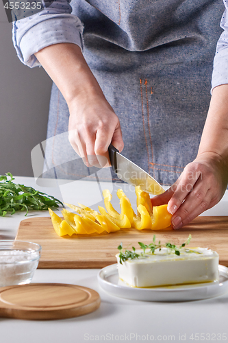 Image of Woman\'s hands are cutting organic peppers on a wooden board on a gray table. Cooking salad.