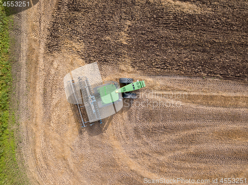 Image of Top view of green tractor plowing the ground after harvesting on the field in the autumn time. Top view.