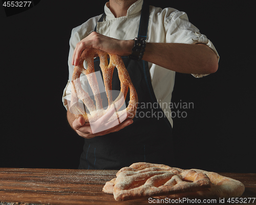 Image of on background of wooden brown table, men\'s hands hold bread foug