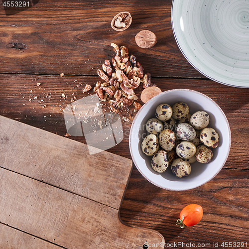 Image of A bowl with quail eggs, pieces of walnut and a wooden board on the kitchen table with copy space. Ingredients for Healthy Salad. Flat lay