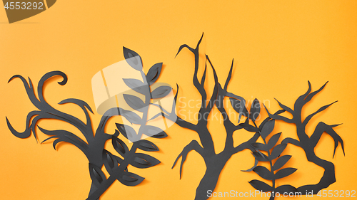 Image of Mystical pattern of black paper handcraft leaves and trees on an orange background with space for text. Halloween layout. Flat lay