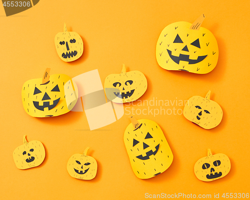 Image of Pattern of a variety of handcraft paper pumpkins with faces on an orange background with space for text. Layout to Halloween. Flat lay