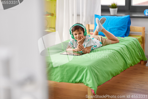 Image of smiling boy with tablet pc and headphones at home