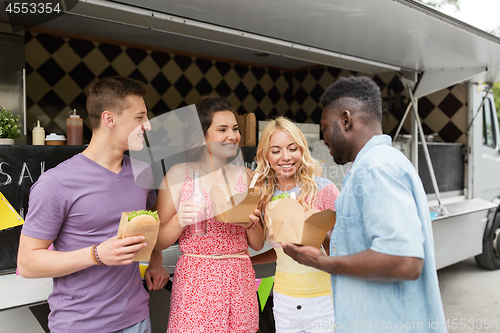 Image of happy friends with drinks eating at food truck