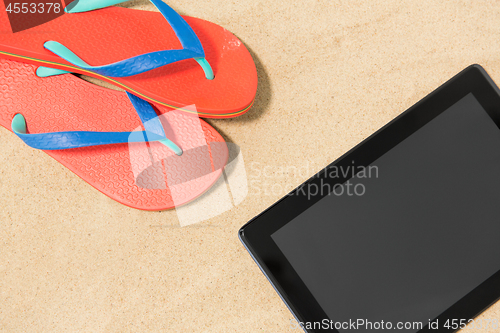 Image of tablet computer and flip flops on beach sand