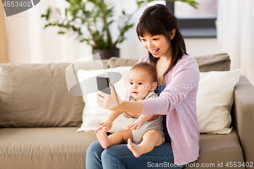 Image of asian mother with baby son taking selfie at home