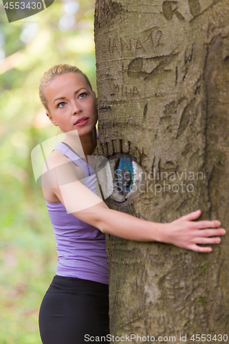 Image of Young woman hugging a tree.