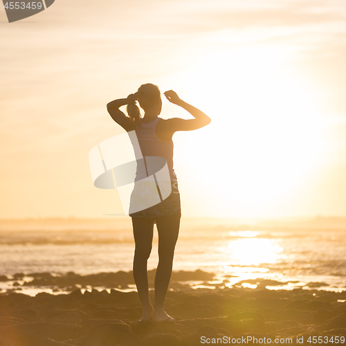 Image of Woman on sandy beach watching sunset.