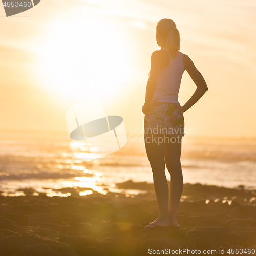 Image of Woman on sandy beach watching sunset.