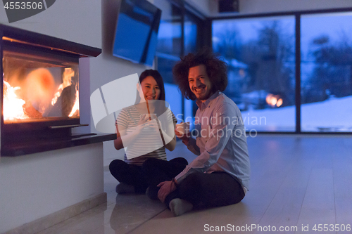 Image of happy multiethnic couple sitting in front of fireplace