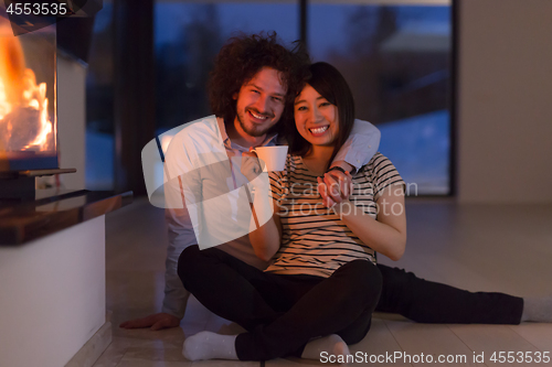 Image of happy multiethnic couple sitting in front of fireplace