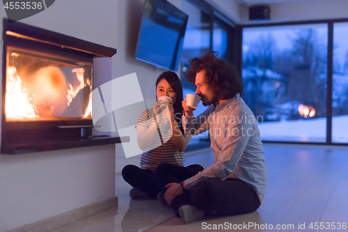 Image of happy multiethnic couple sitting in front of fireplace