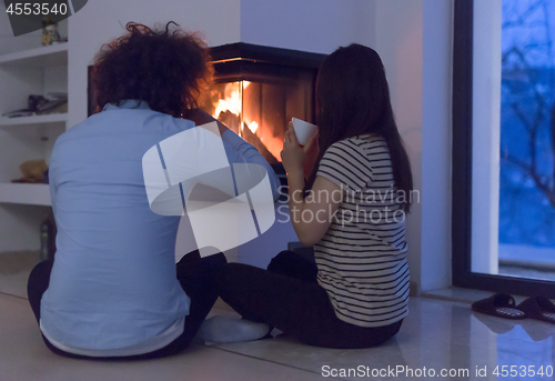 Image of happy multiethnic couple sitting in front of fireplace