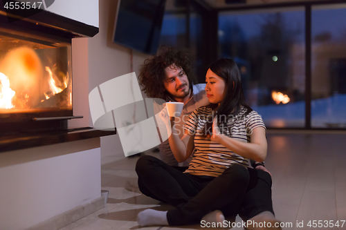 Image of happy multiethnic couple sitting in front of fireplace