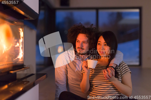 Image of happy multiethnic couple sitting in front of fireplace