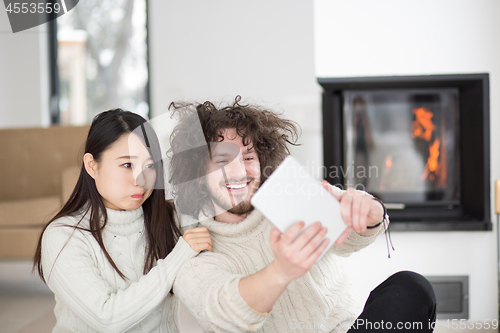 Image of multiethnic couple using tablet computer in front of fireplace