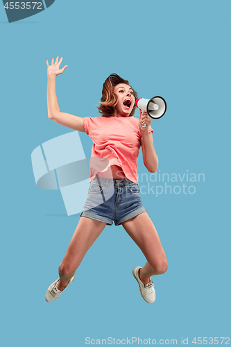 Image of Beautiful young woman jumping with megaphone isolated over blue background