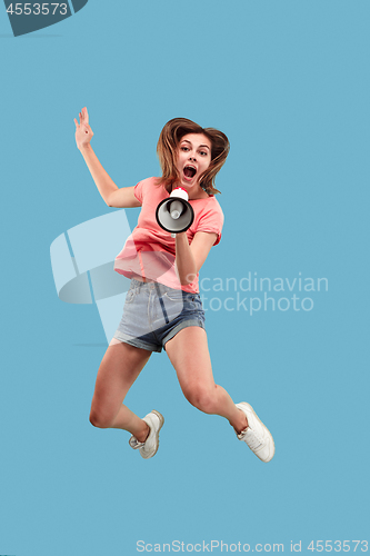 Image of Beautiful young woman jumping with megaphone isolated over blue background