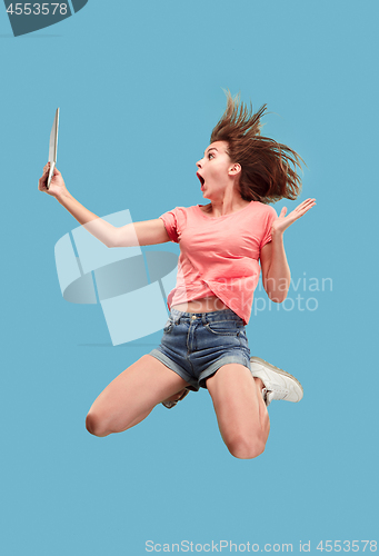 Image of Image of young woman over blue background using laptop computer or tablet gadget while jumping.