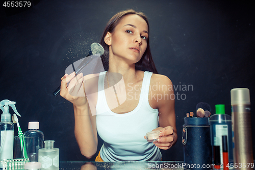 Image of Beauty woman applying makeup. Beautiful girl looking in the mirror and applying cosmetic with a big brush.