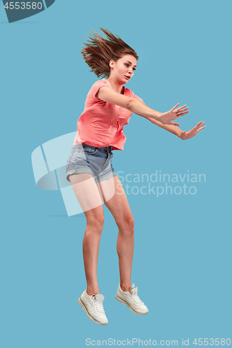 Image of Freedom in moving. Pretty young woman jumping against blue background