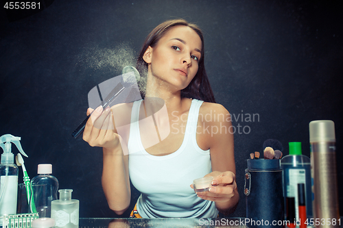 Image of Beauty woman applying makeup. Beautiful girl looking in the mirror and applying cosmetic with a big brush.